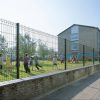 Many kids are playing around in the leisure park enclosed by curvy welded fence